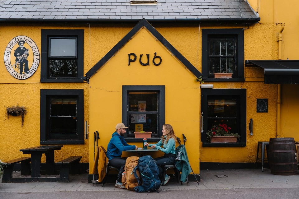 People sitting outside of a bright yellow pub along the Kerry Way 