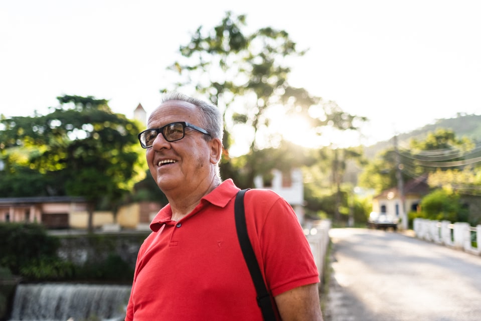 An older man with glasses and a red shirt smiling outdoors.