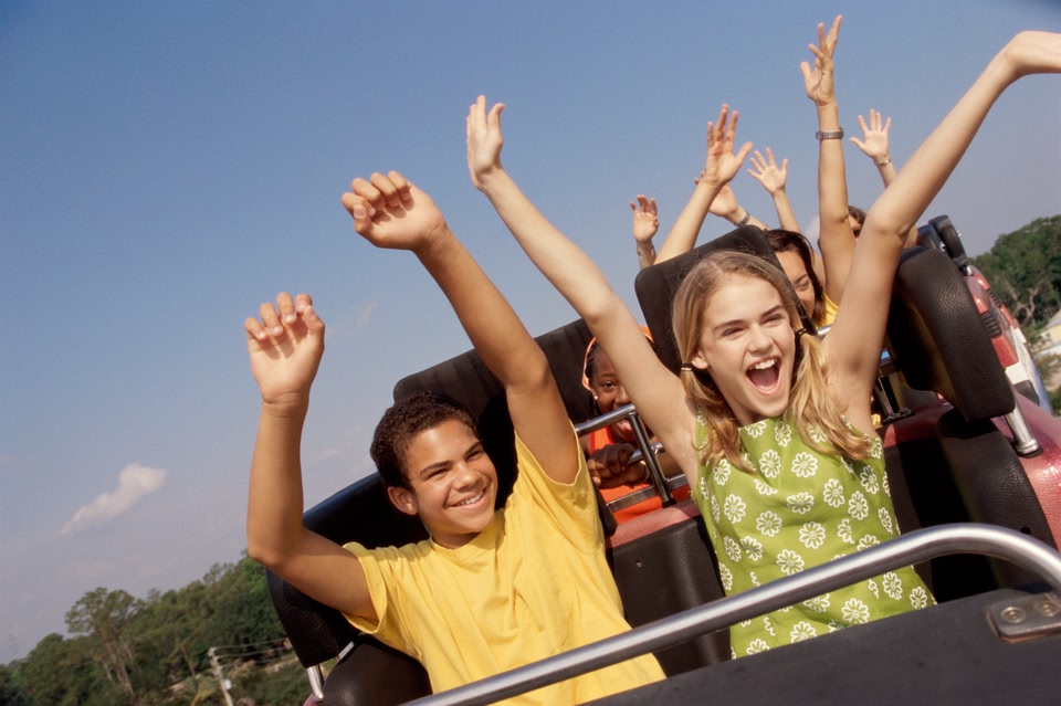 A boy and girl sitting next to each other on a rollercoaster with their hands in the air.
