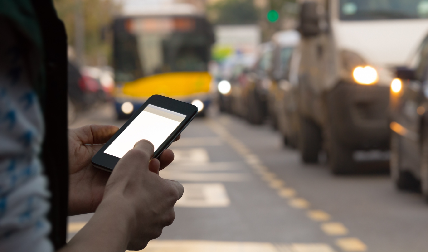 person on their smartphone outside standing on the side of traffic