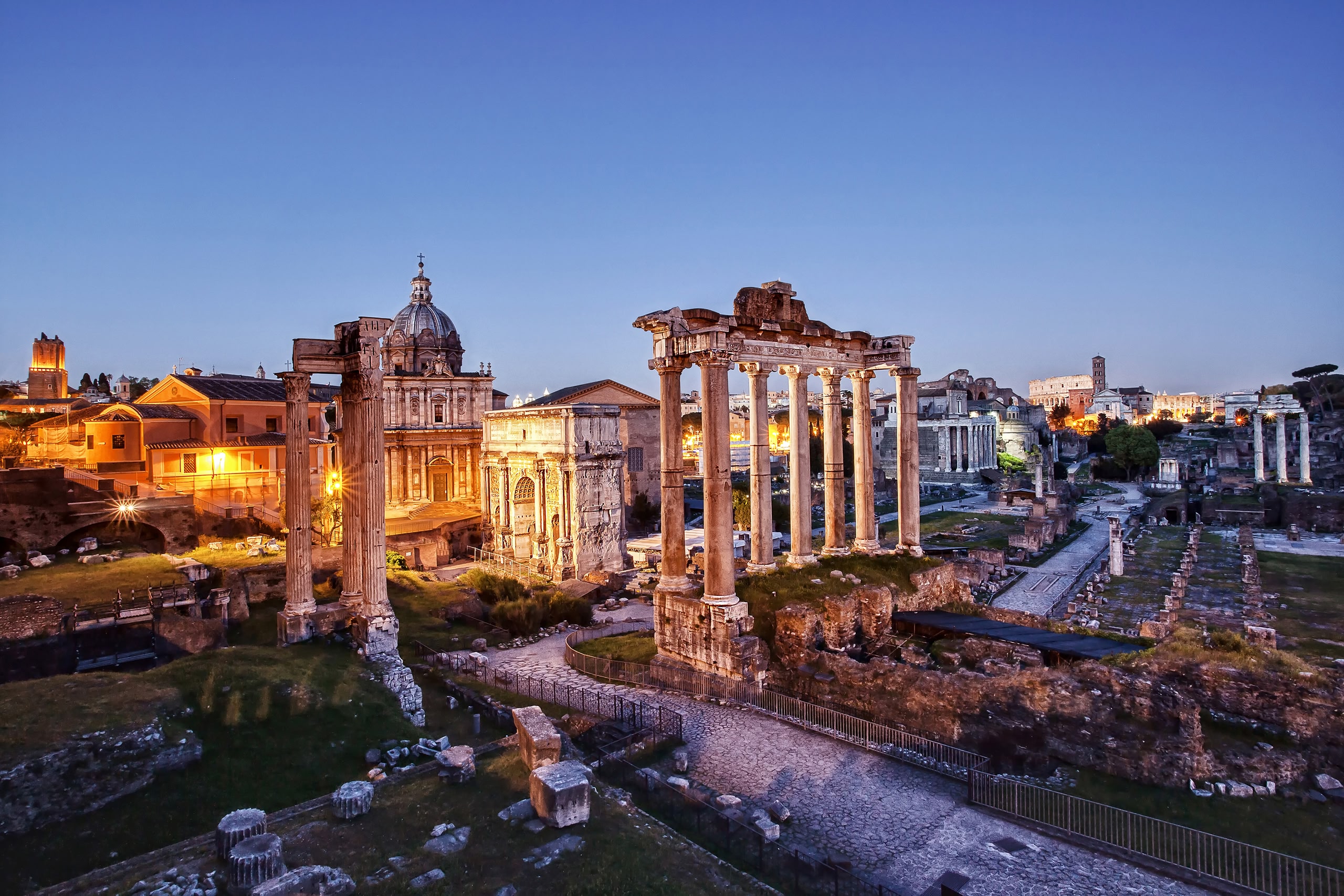 The Roman Forum photographed at sunset, with artificial lights on.The Roman Forum: Left the Temple of Vespasian, the Arch of Septimius Severus and the Temple of Saturn. Rightmost the plaza of the Basilica Giulia front of the three columns of the Temple of Castor and Pollux and the Palatine Hill.