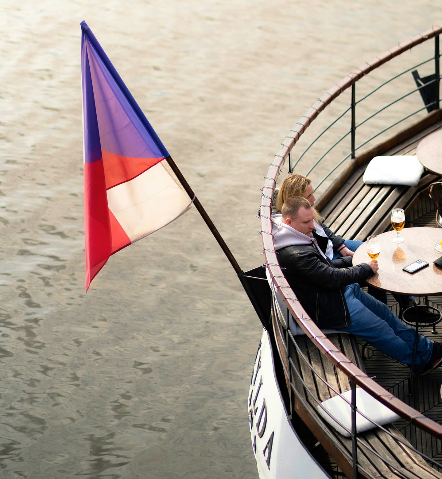 Para pijąca drinki w łodzi zacumowanej na nadbrzeżu w Pradze. Widać flagę Czech.