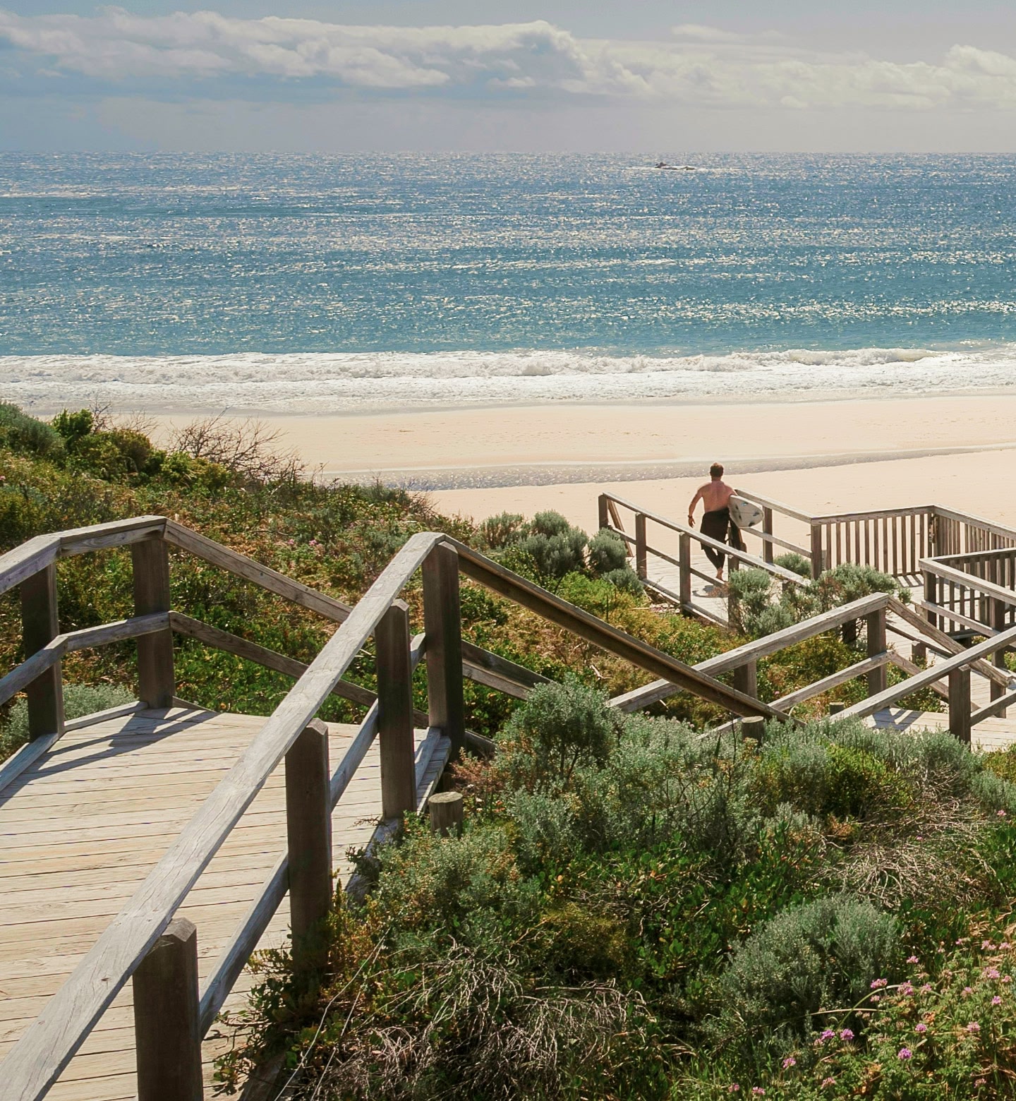 Surfer walks towards beach from boardwalk in Broome Australia