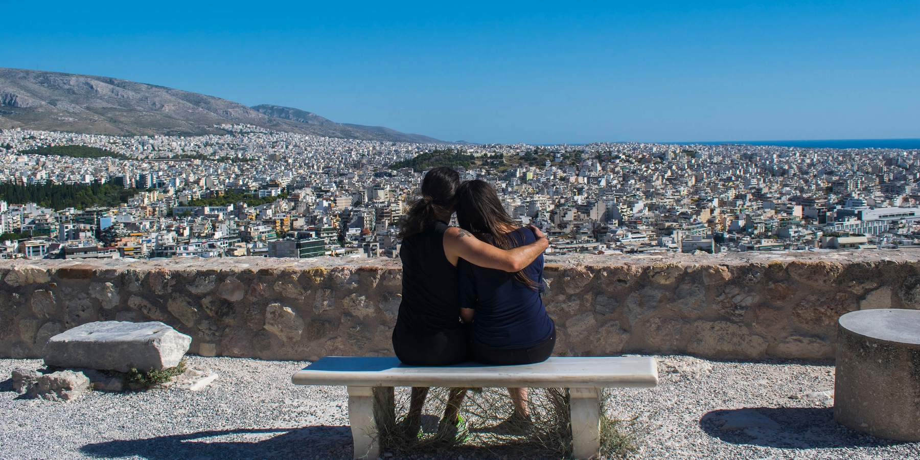 Two people on a bench hugging looking over a Greek city