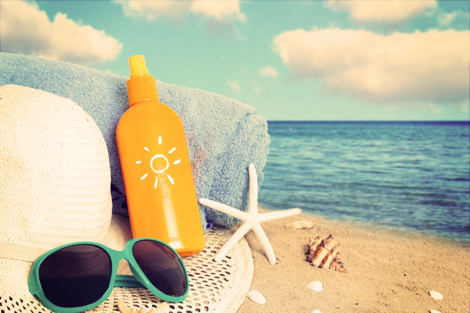 Bottle of suntan lotion, glasses, hat and towel on the beach