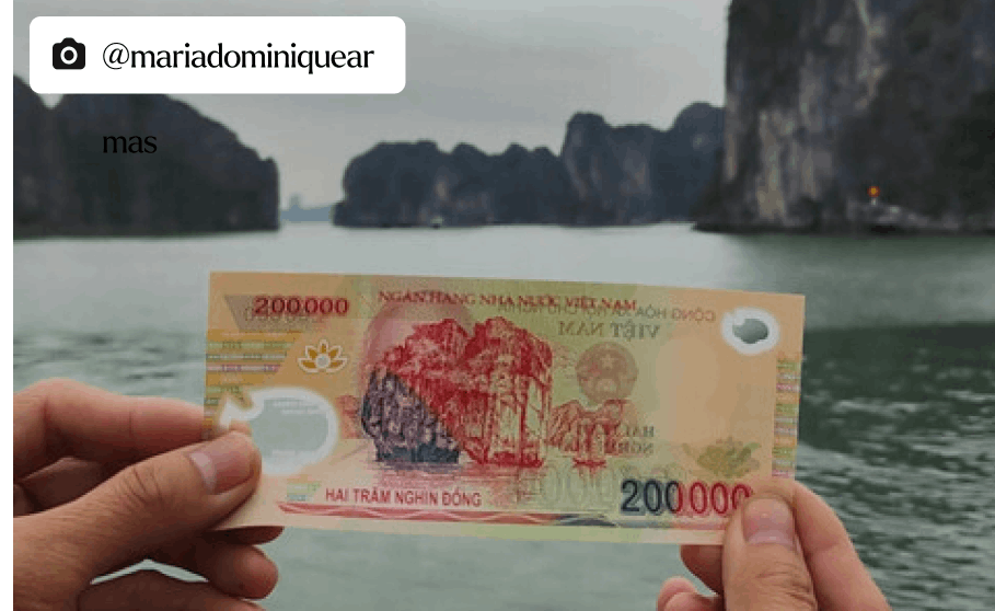 A person holding up a 200,000 Vietnamese Dong note in Ha Long bay on a boat. 