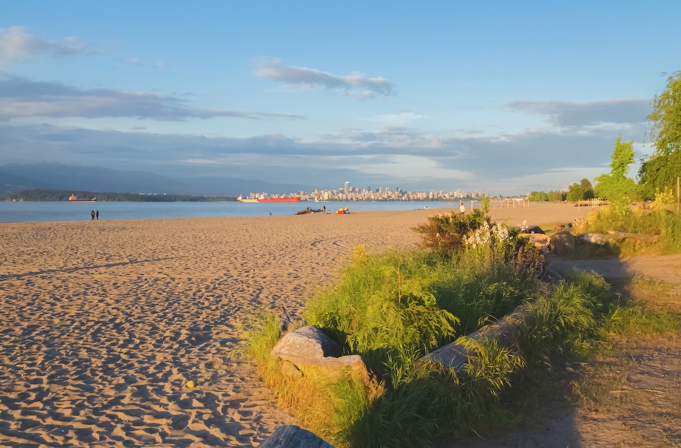 golden sand at Spanish Banks Beach in Vancouver, city skyline in the background and blue afternoon sky.