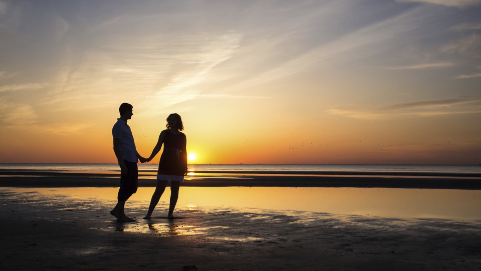 A man and a women holding hands on a beach at sunset