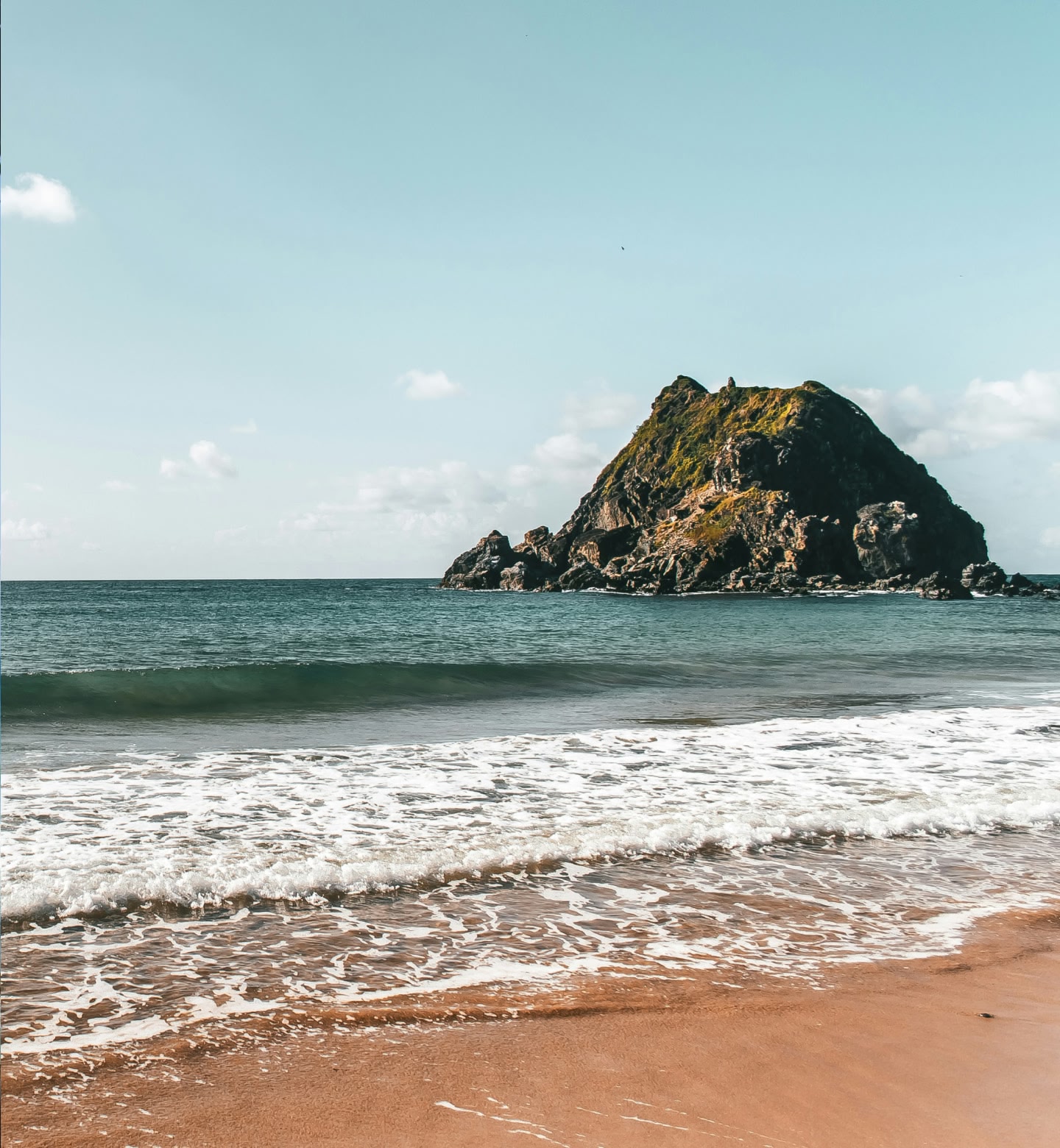 Uma pequena ilha rochosa no oceano calmo com ondas suaves perto de Fernando de Noronha, Brasil.