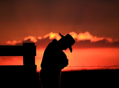 Uma silhueta de um homem contra um pôr do sol usando um chapéu estilo cowboy