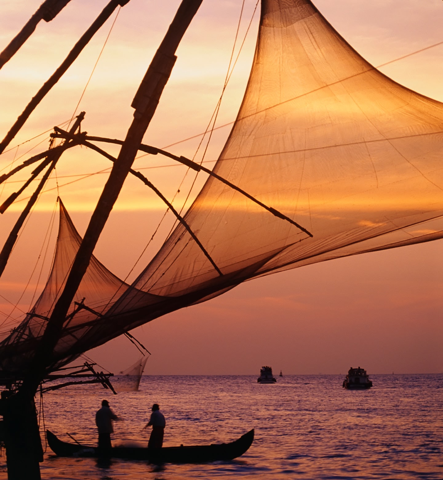 Die Silhouetten von Fischern, die bei Sonnenuntergang vor der Küste von Kochi, Indien, große Netze ins Meer werfen.