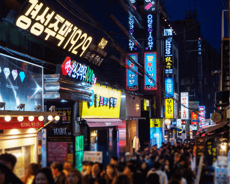 A vibrant night scene on a bustling street illuminated by colorful neon signs, with a lively crowd of people filling the energetic atmosphere.