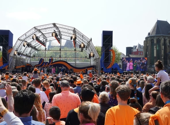 A large crowd gathered in front of a stage for a festival in Amsterdam during King's Day.