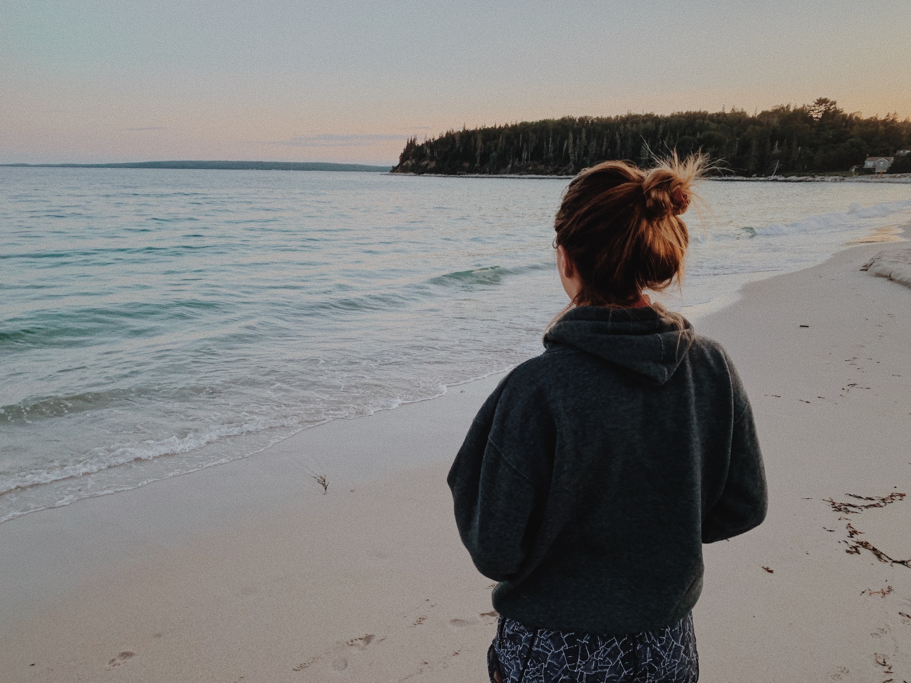 person with their hair in a bun standing and looking out at the shores of Lawrencetown Beach in Halifax at sunset
