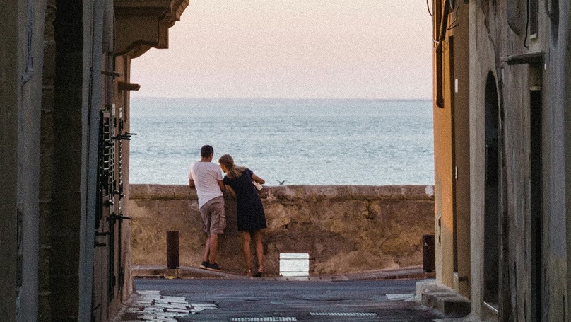 Una coppia si trova alla fine di una strada stretta, guardando il mare.