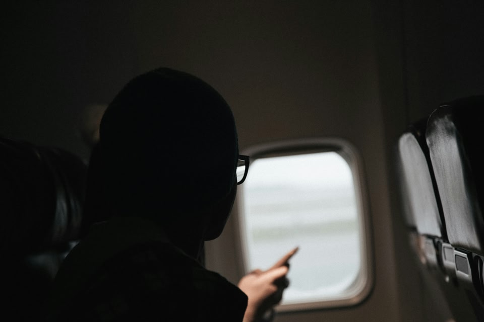 A woman with long wavy hair gazes thoughtfully out of an airplane window at a bright sky during a flight.