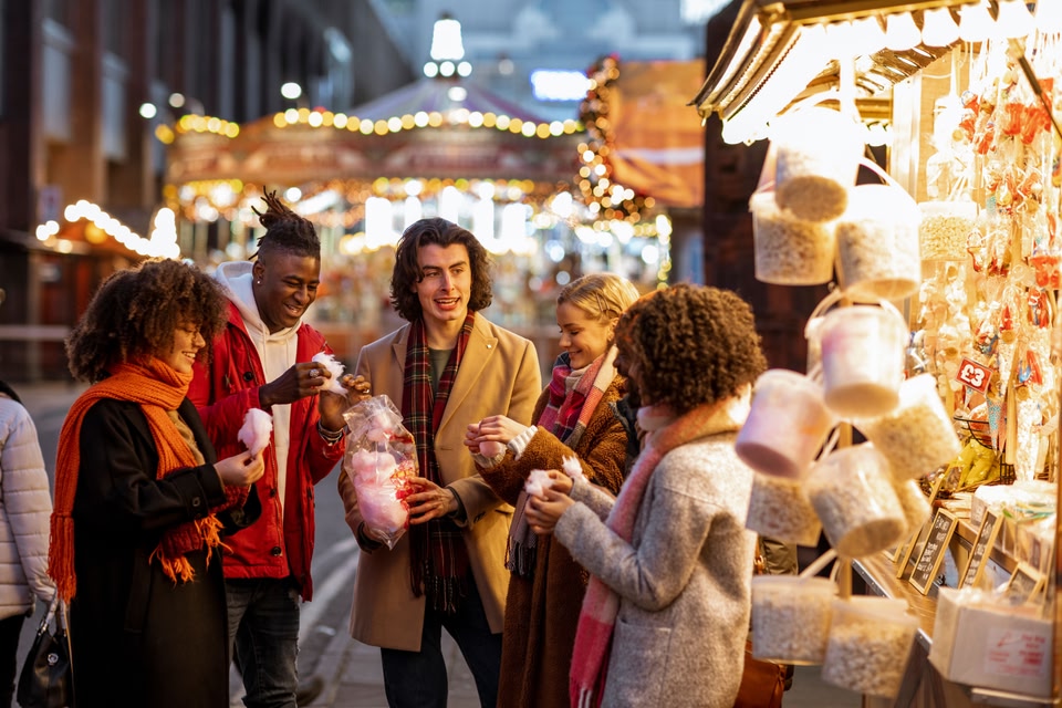 Side view of a group of friends sharing a bag of cotton candy at the Christmas market in Newcastle upon Tyne in the north-east of England.