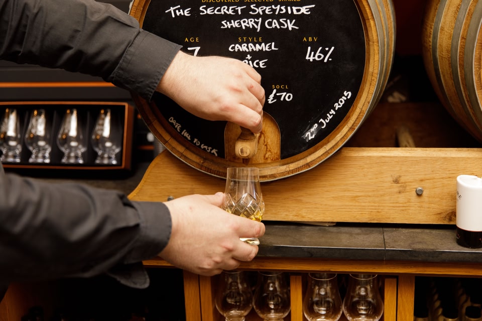 A man pours a dram of whisky from a barrel at The Whisky Shop, Edinburgh, 2022.