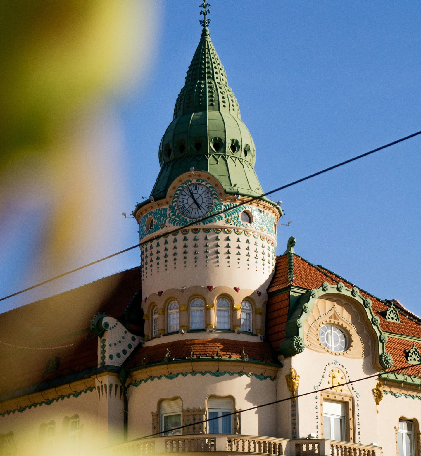 Ein kunstvoll verzierter Glockenturm mit grüner Kuppel unter strahlend blauem Himmel in Oradea (Großwardein), Rumänien.