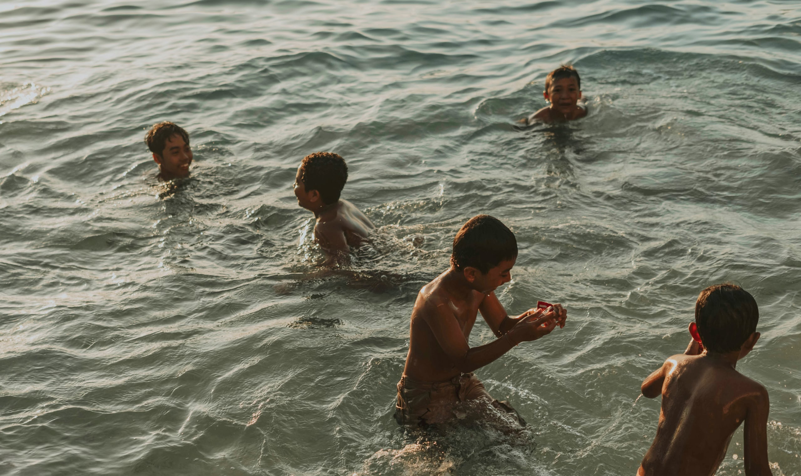 Cinco niños pequeños juegan en el mar.