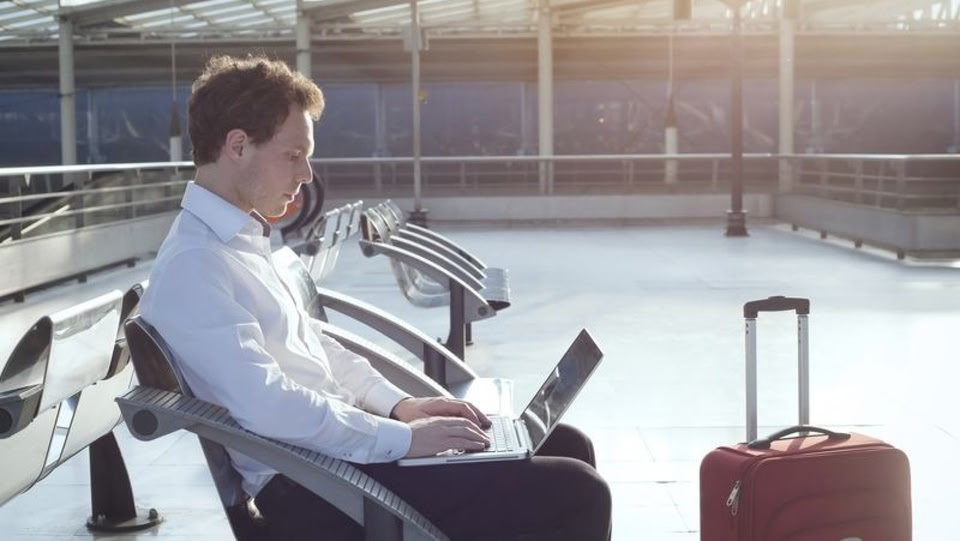 Ein Mann sitzt mit seinem Koffer in einem Flughafenterminal und arbeitet an seinem Laptop.