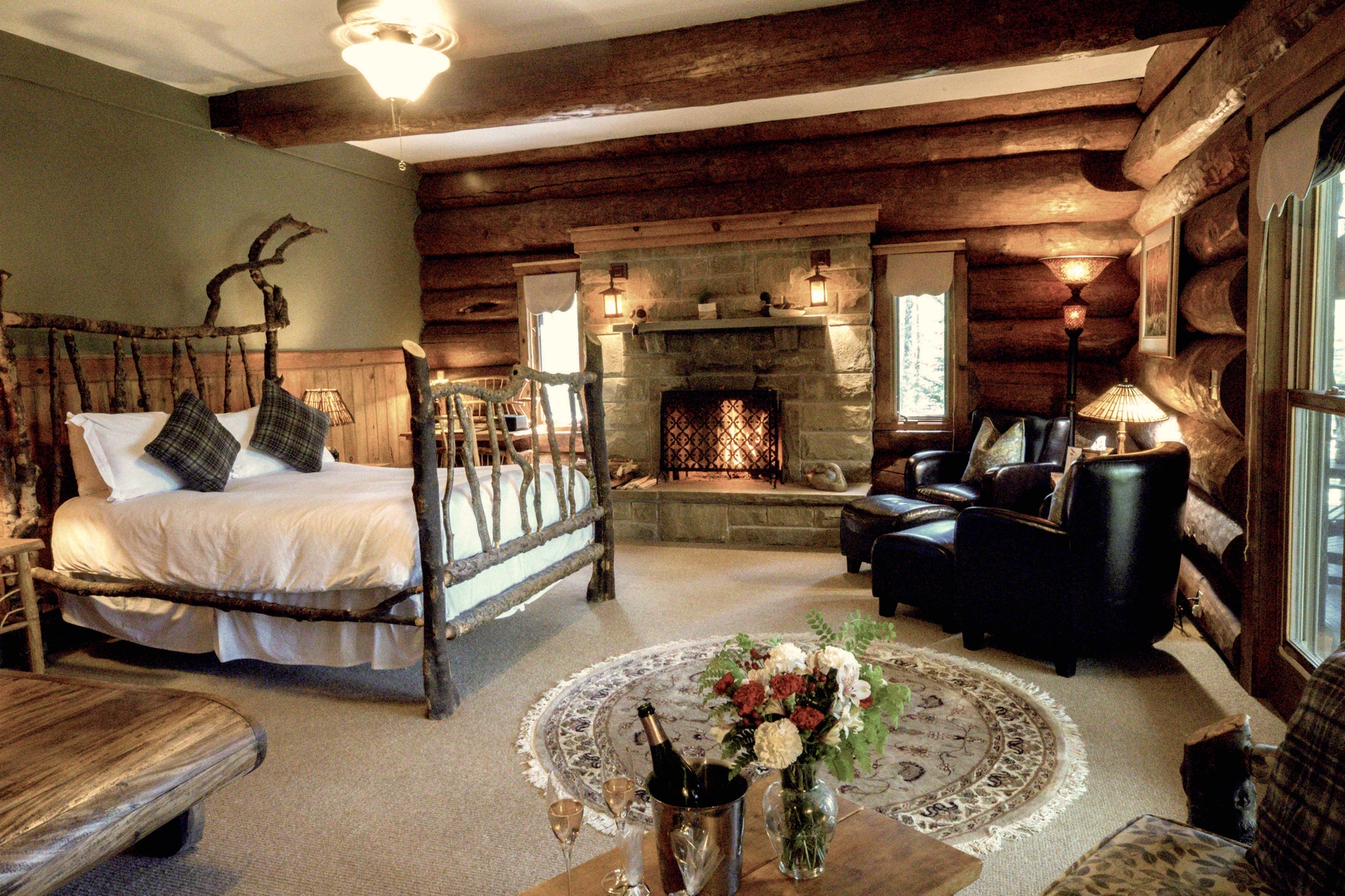 cozy suite in Trout Point Lodge. Bed, fireplace, table with a bottle of champagne and two glasses poured.