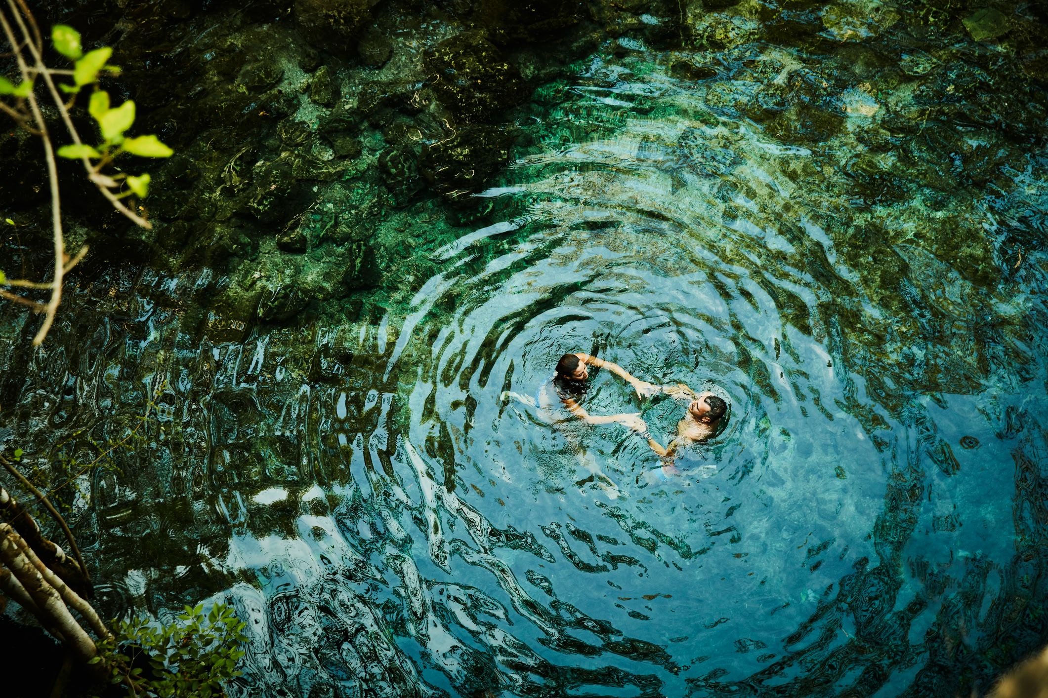 Overhead view of couple holding hands while swimming in a cenote in Mexico while on vacation.