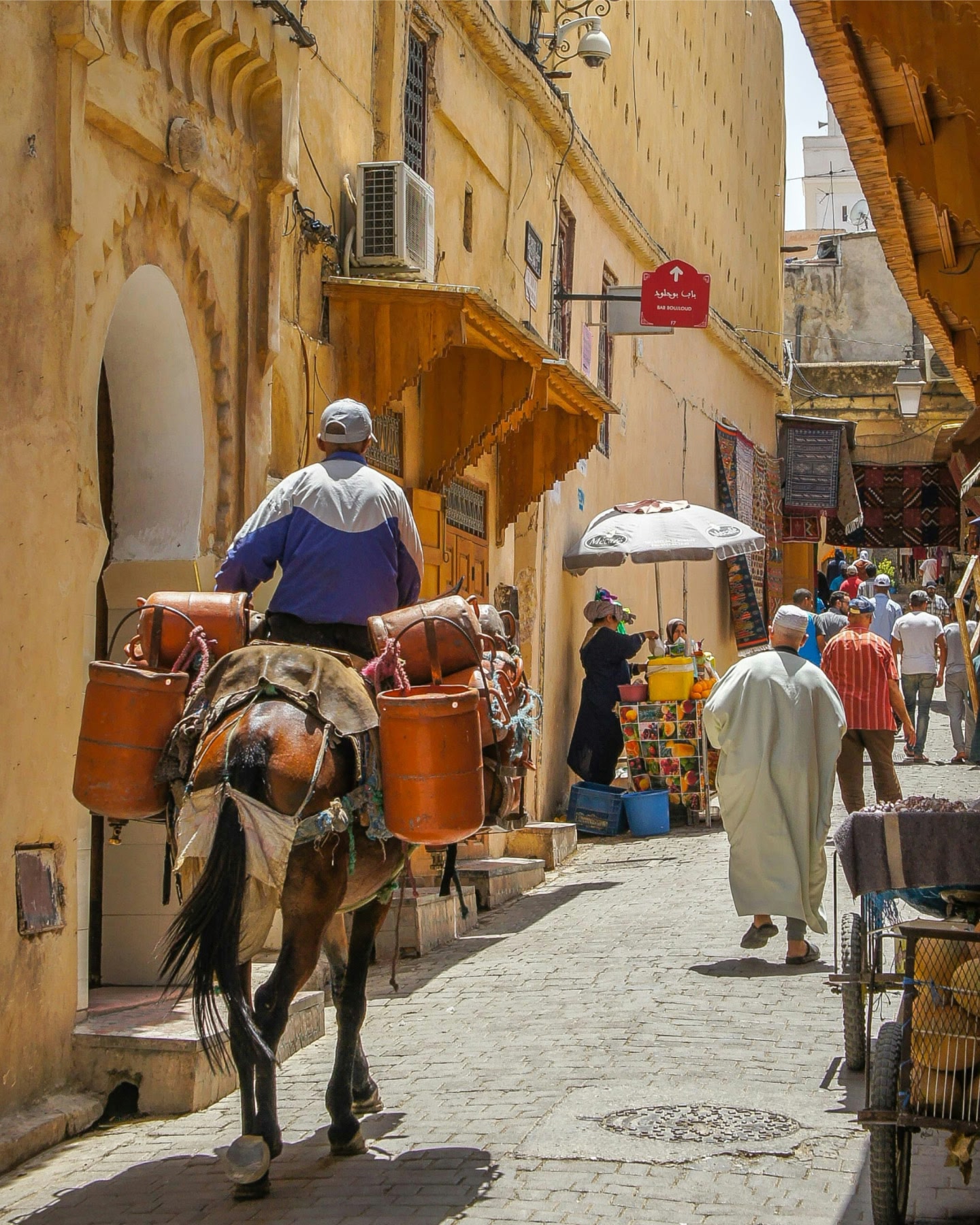 Un cavallo che trasporta sul dorso un uomo e dei contenitori attraverso una strada soleggiata del mercato a Fes, in Marocco.