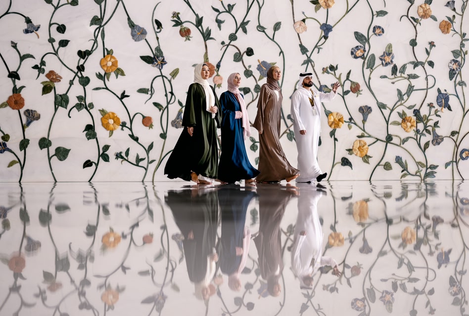 Un groupe de trois femmes et un homme visitent la Grande Mosquée Sheikh Zayed avec ses murs fleuris et son sol réfléchissant.