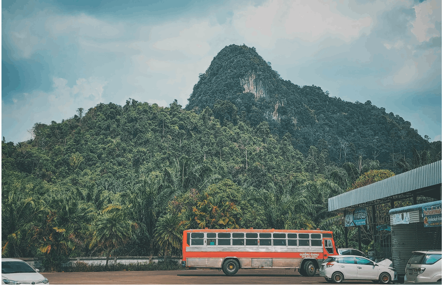 A red and white bus is parked on the roadside against a scenic backdrop of majestic mountains and lush forests.