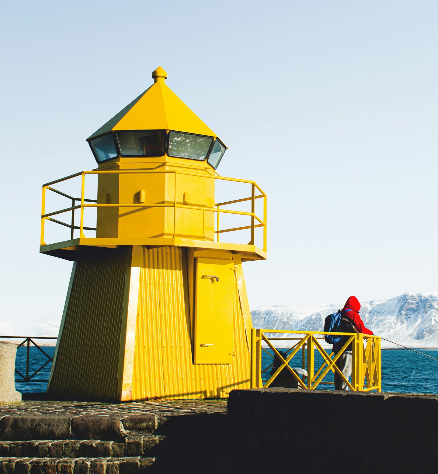 Een eenzame gele vuurtoren met uitzicht op de ijskoude zee en besneeuwde toppen in Reykjavik.