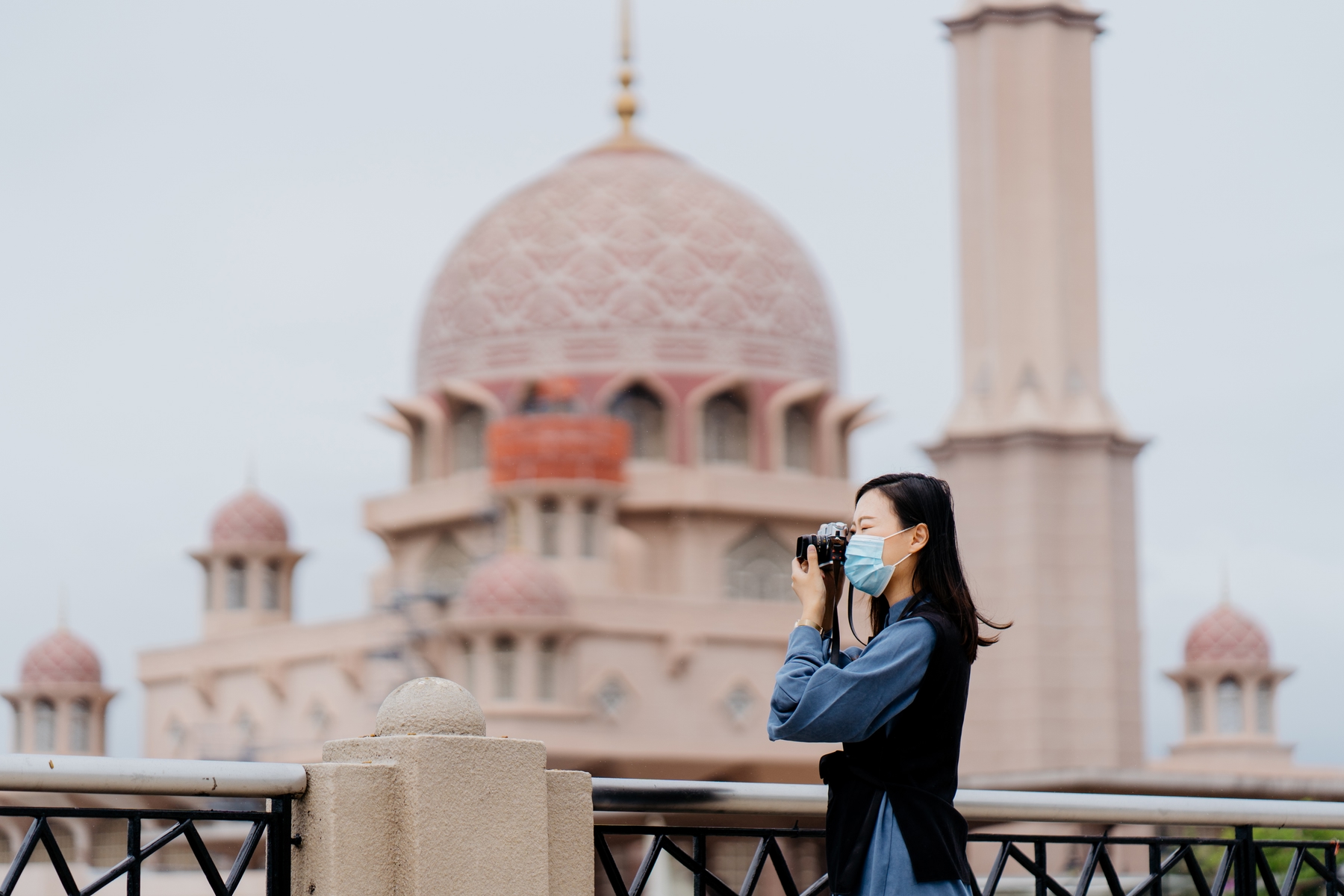 Jovem asiática de máscara fotografando um ponto turístico.