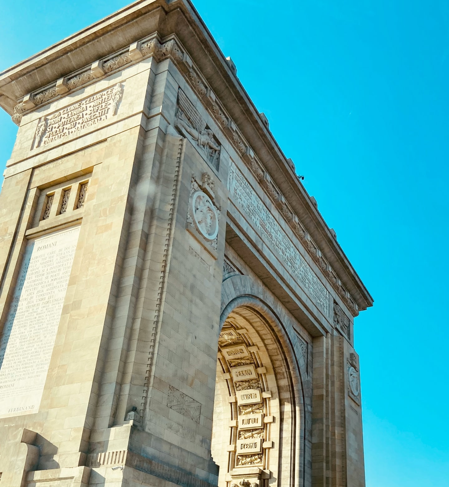 An intricate stone arch in Bucharest, Romania, on a clear sunny day.