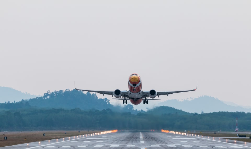 Airplane in flight just above the runway with trees in the background.