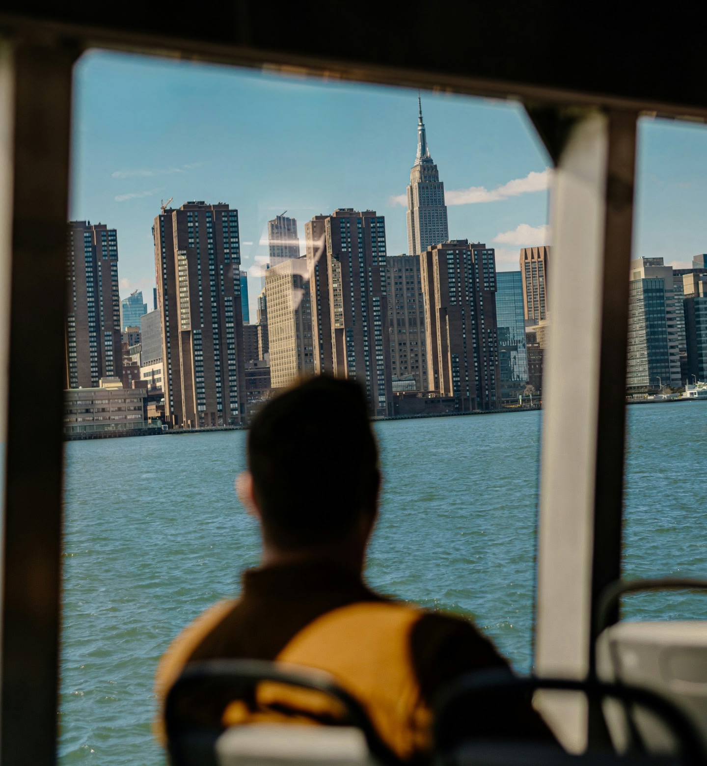A man sits in boat looking across the sea at the New York city skyline on a sunny day in the United States