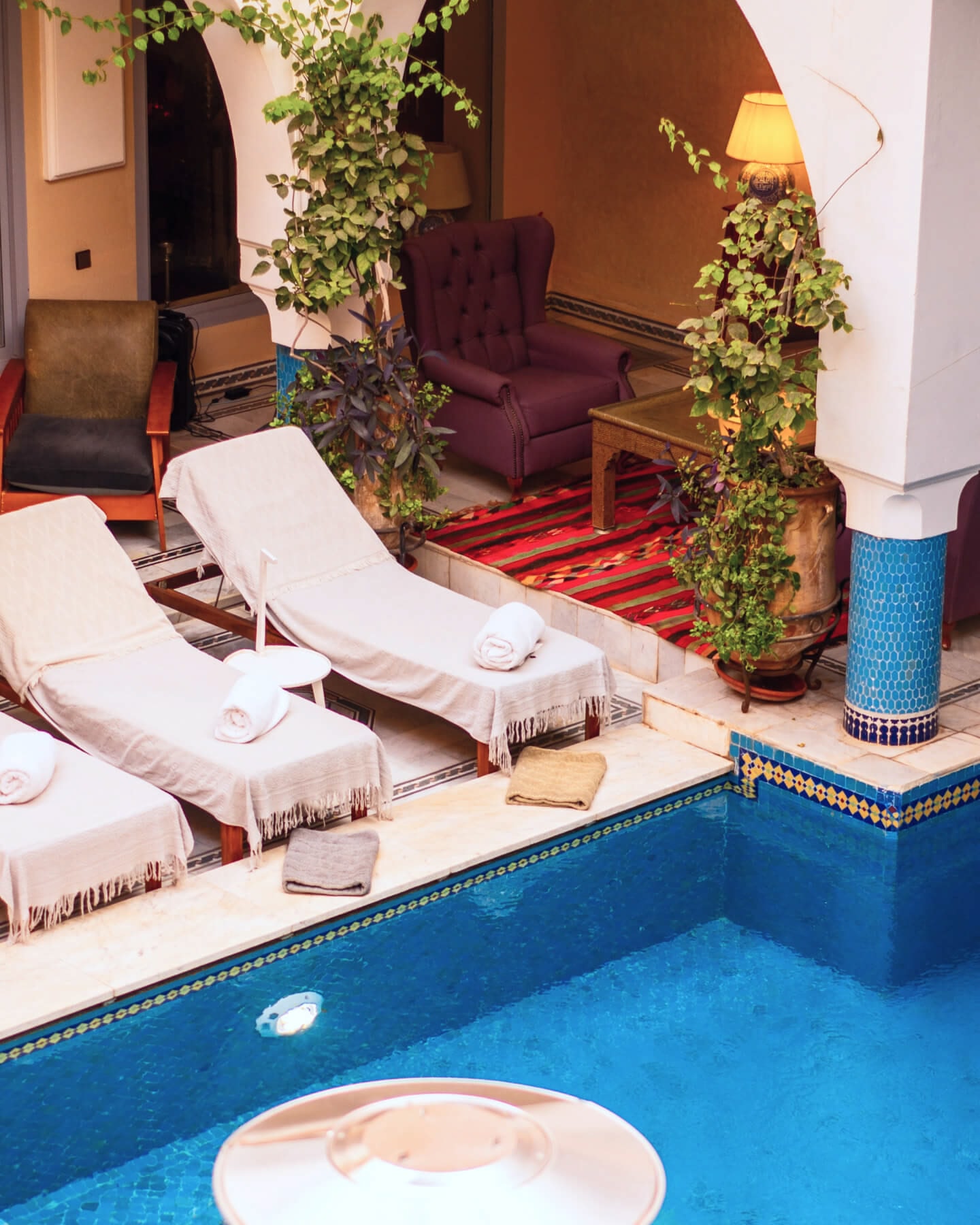 Moroccan pool with blue tiles, red carpets and loungers with cream towels