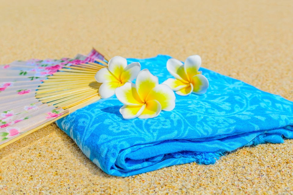 A beach towel, fan and flower accessory.