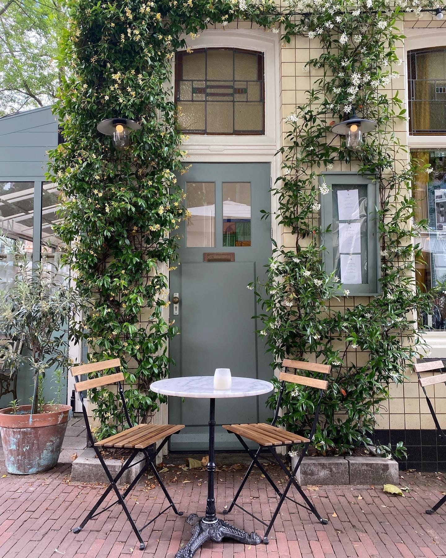 Ivy-clad cafe in Amsterdam with a table and chairs outside.