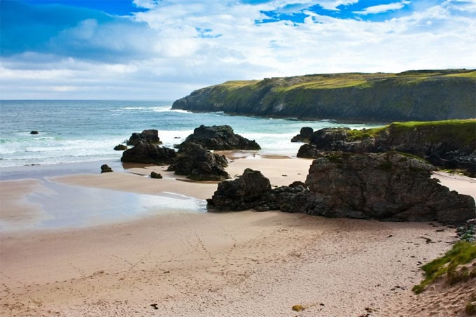 Strand met rotspartijen, golvende zee en groen landschap op de achtergrond, Durness Schotland