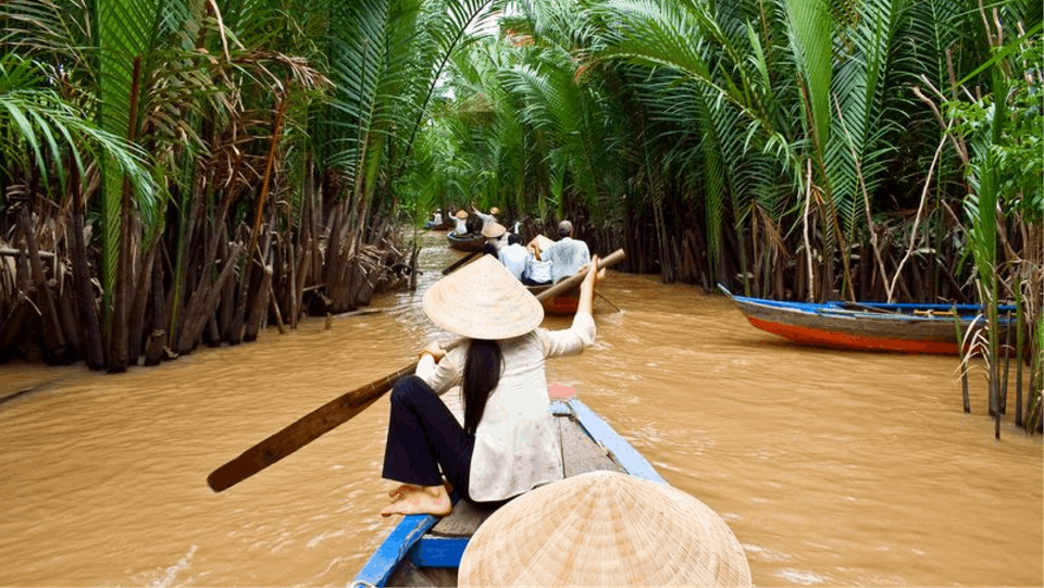 A group of Vietnamese canoes paddling down a small river flanked by high bamboo plants