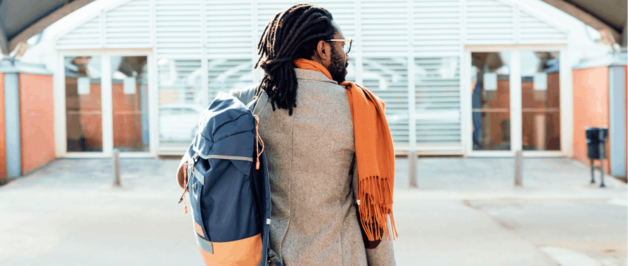 A man waiting for a taxi dressed in an orange scarf and wearing a rucksack