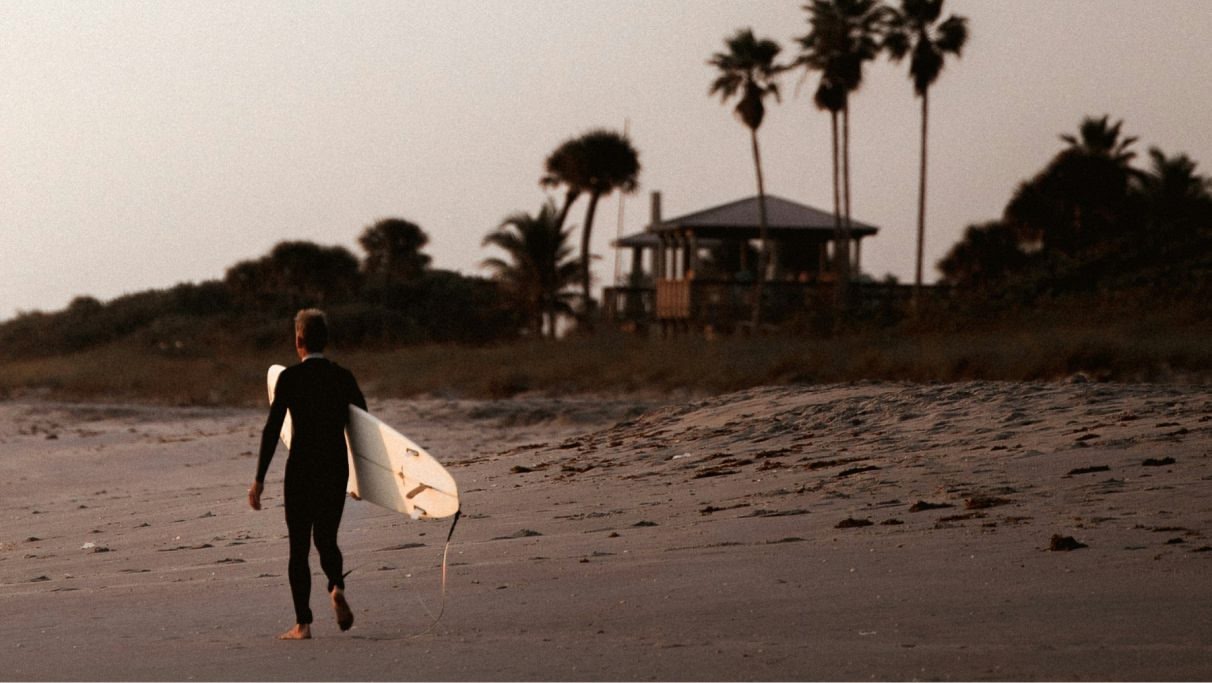 Ein Mann geht am Strand entlang und trägt ein Surfbrett bei Tag.