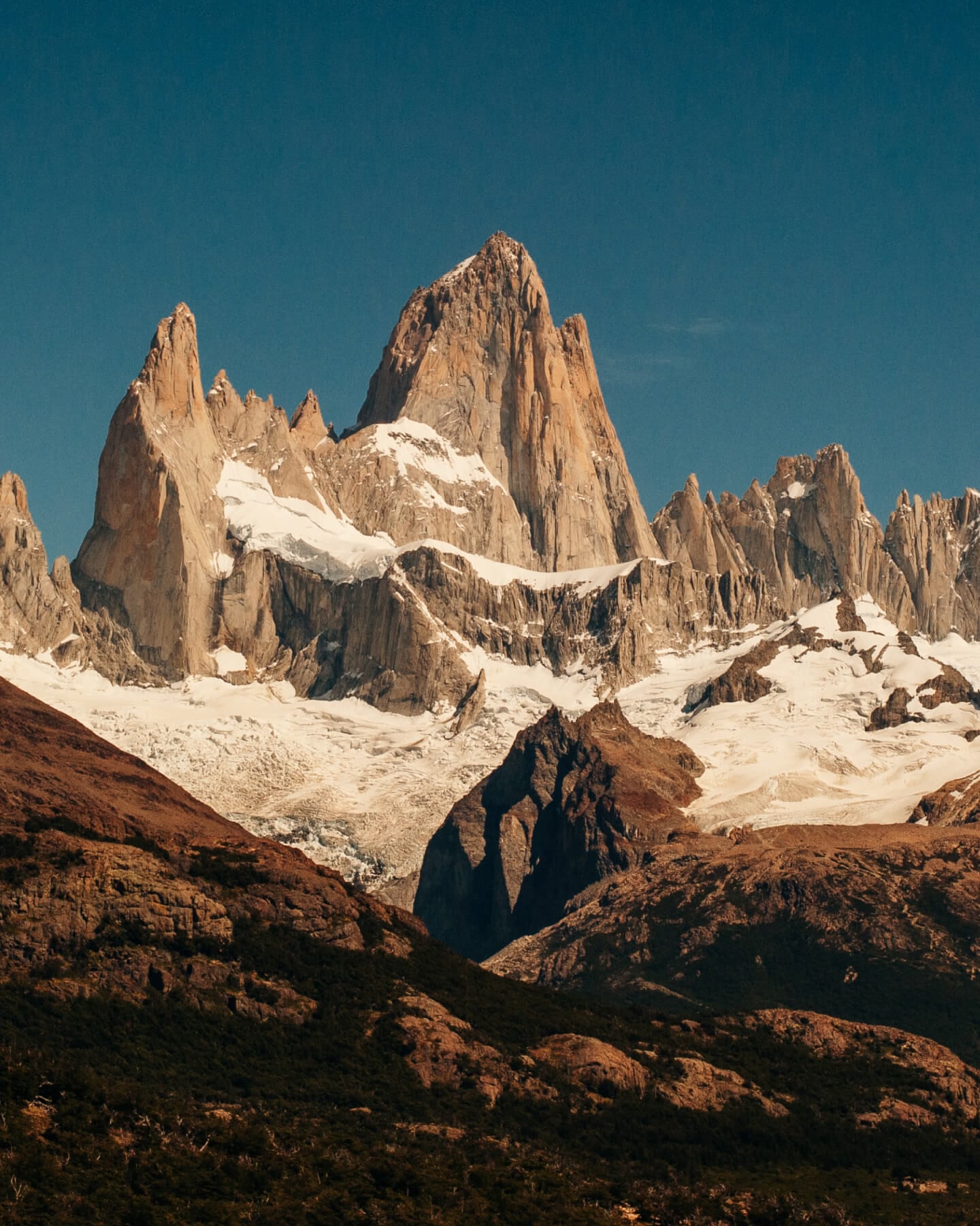 Rocky mountain peaks with snow around them against a dark blue sky