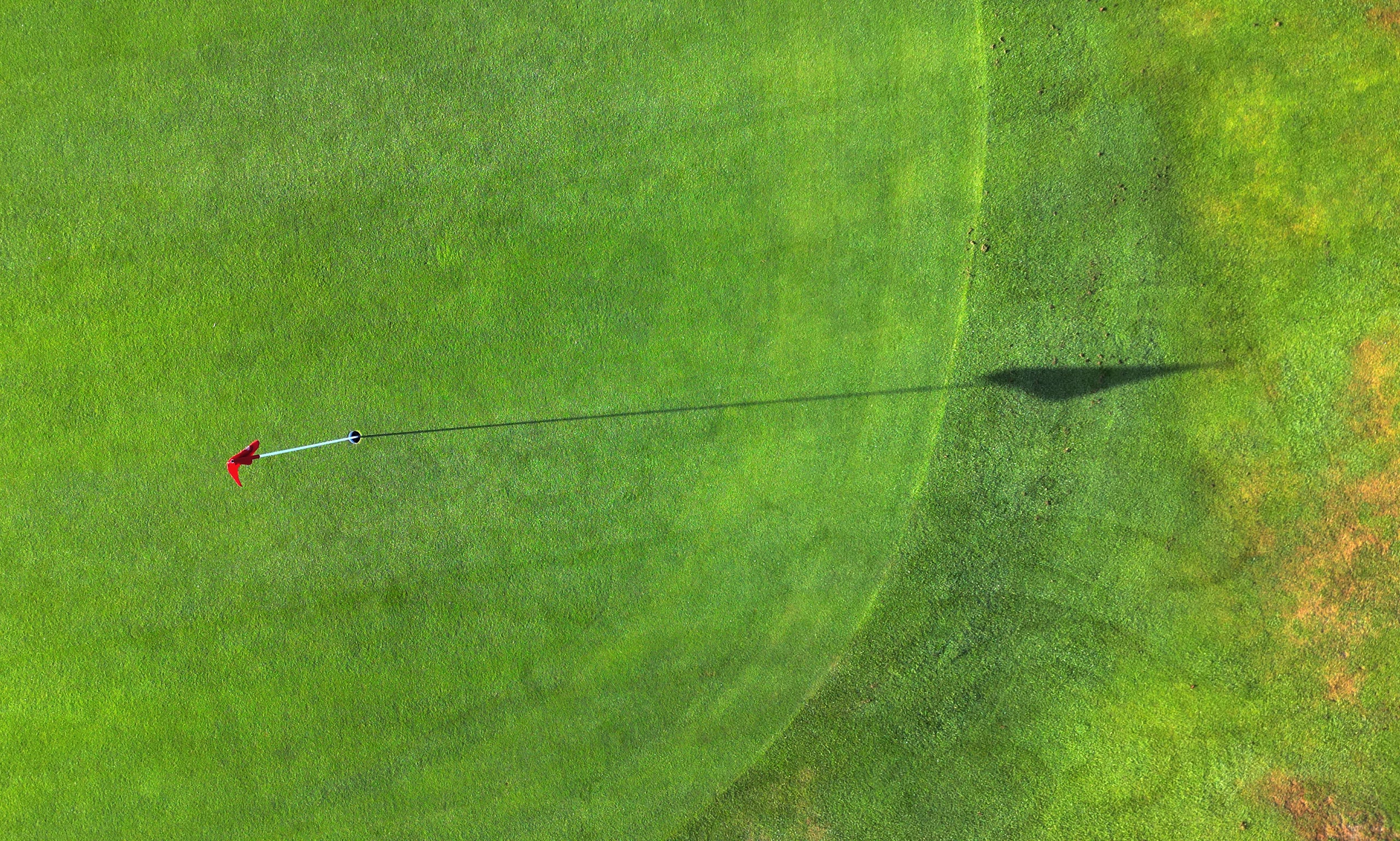 Overhead aerial view of a red golf flag and shadow on a putting green