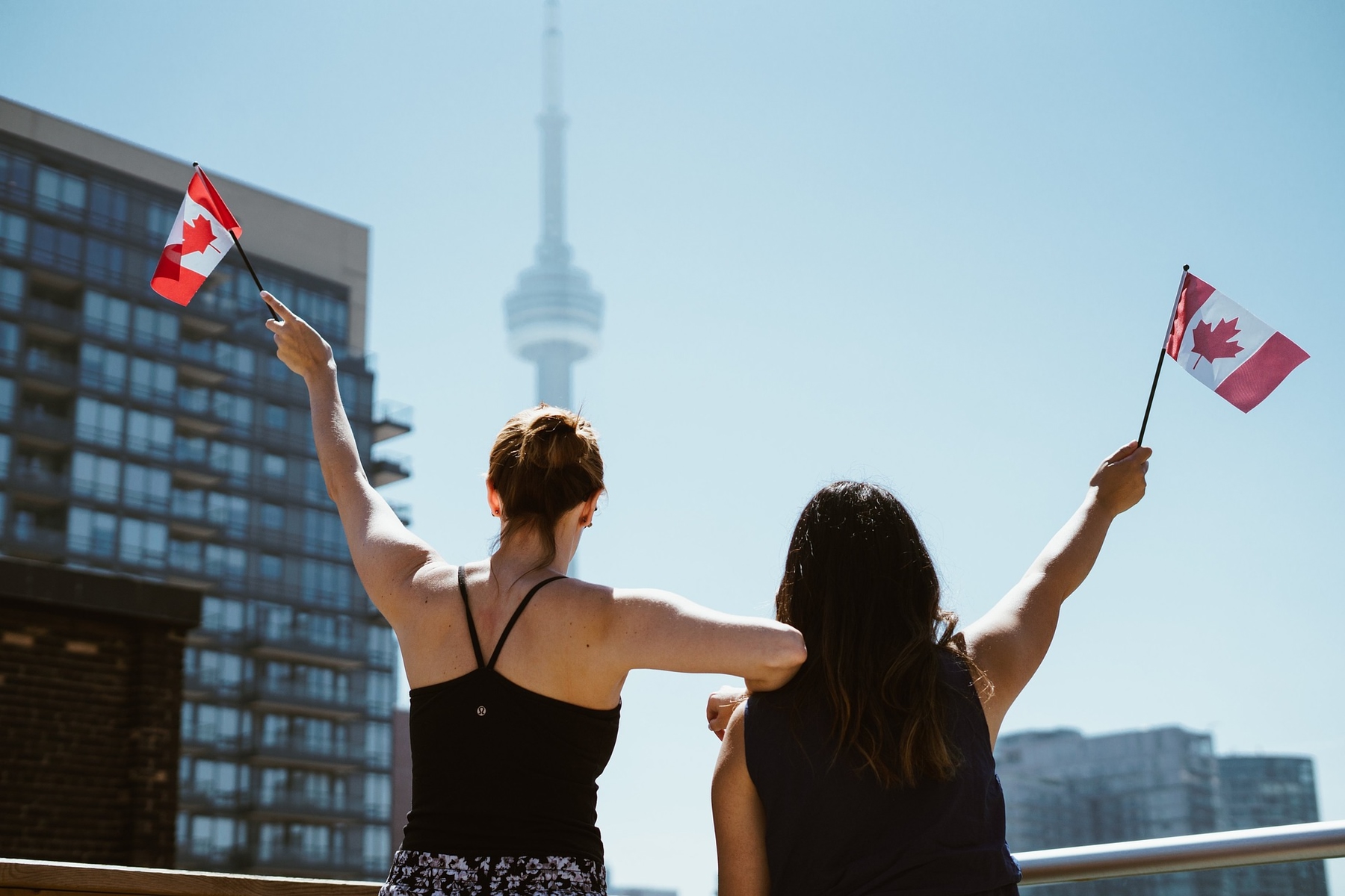 two women holding Canadian flags with the CN Tower in the background