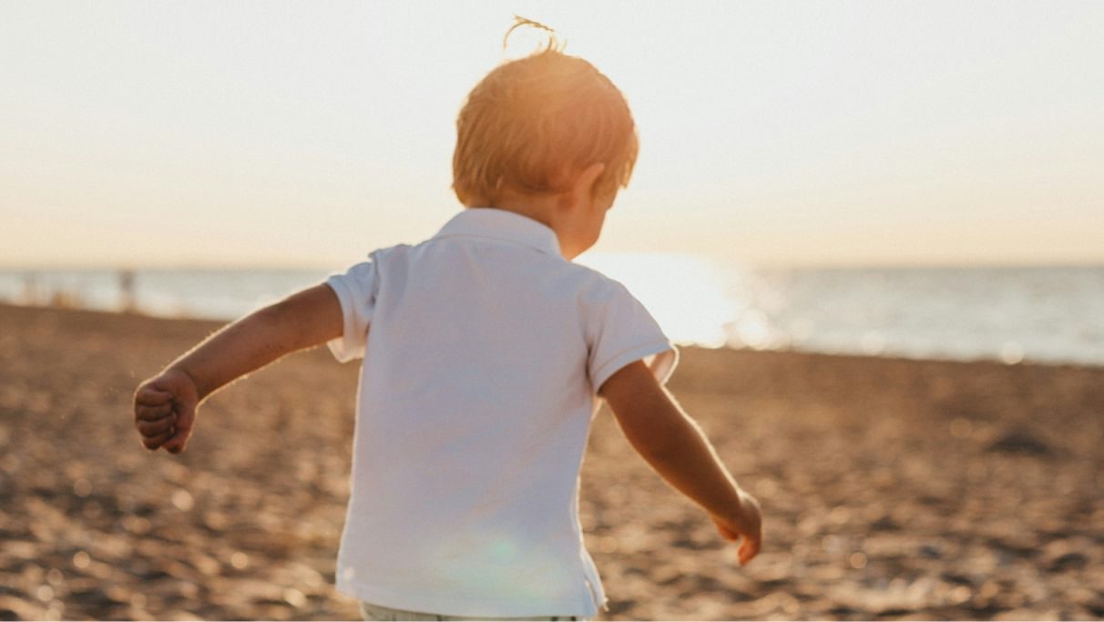 immagine di un bambino di spalle che cammina in spiaggia verso il mare di giorno. 