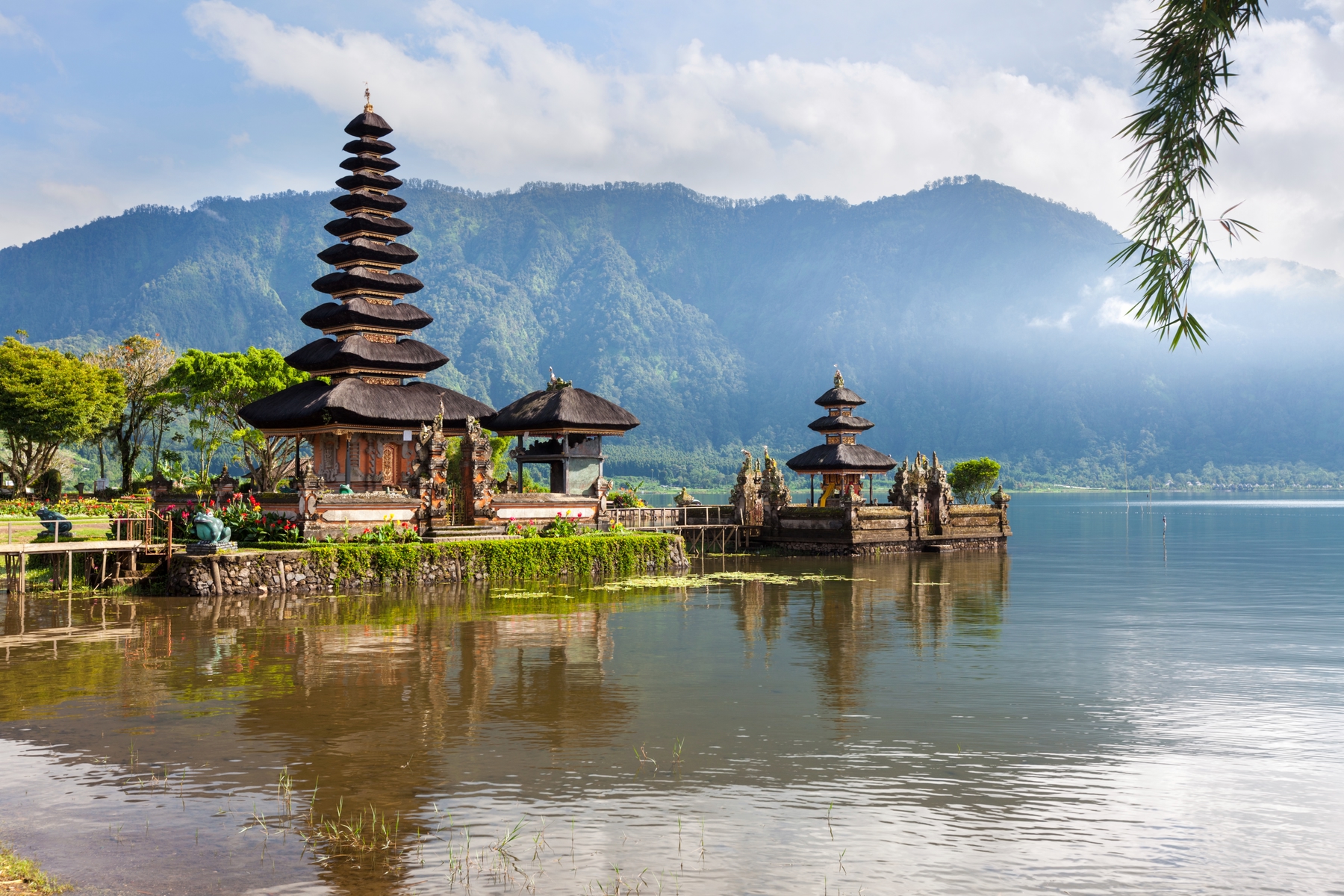 A temple in Bali, jutting out into a placid lake with with atmospheric misty mountains in the background