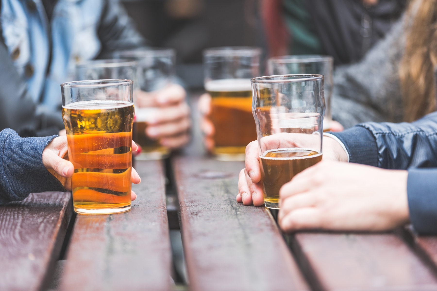 People holding beers are gathered around a table outdoors.