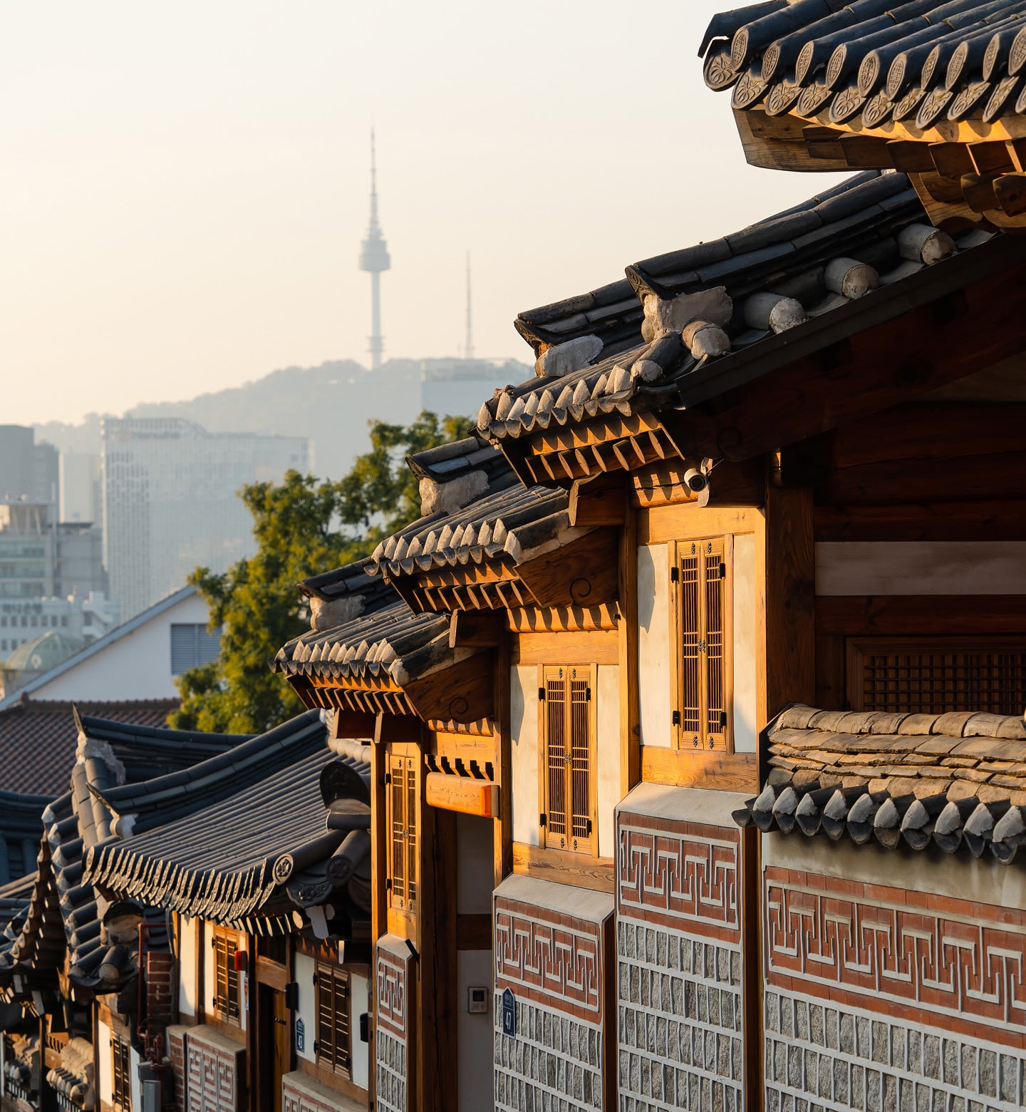 The sun lights up ornate houses with distinctive South Asian roofs against a background of the cityscape of Seoul, South Korea