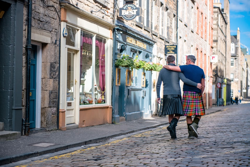Same sex male couple wearing kilts walking arm in arm along Thistle Street, Edinburgh, Scotland.